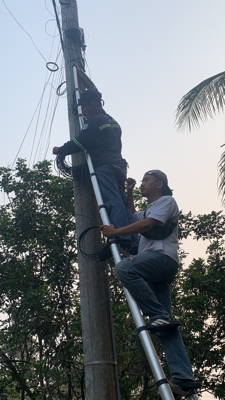 Teknisi menarik dan merapikan kabel jaringan pada tiang
