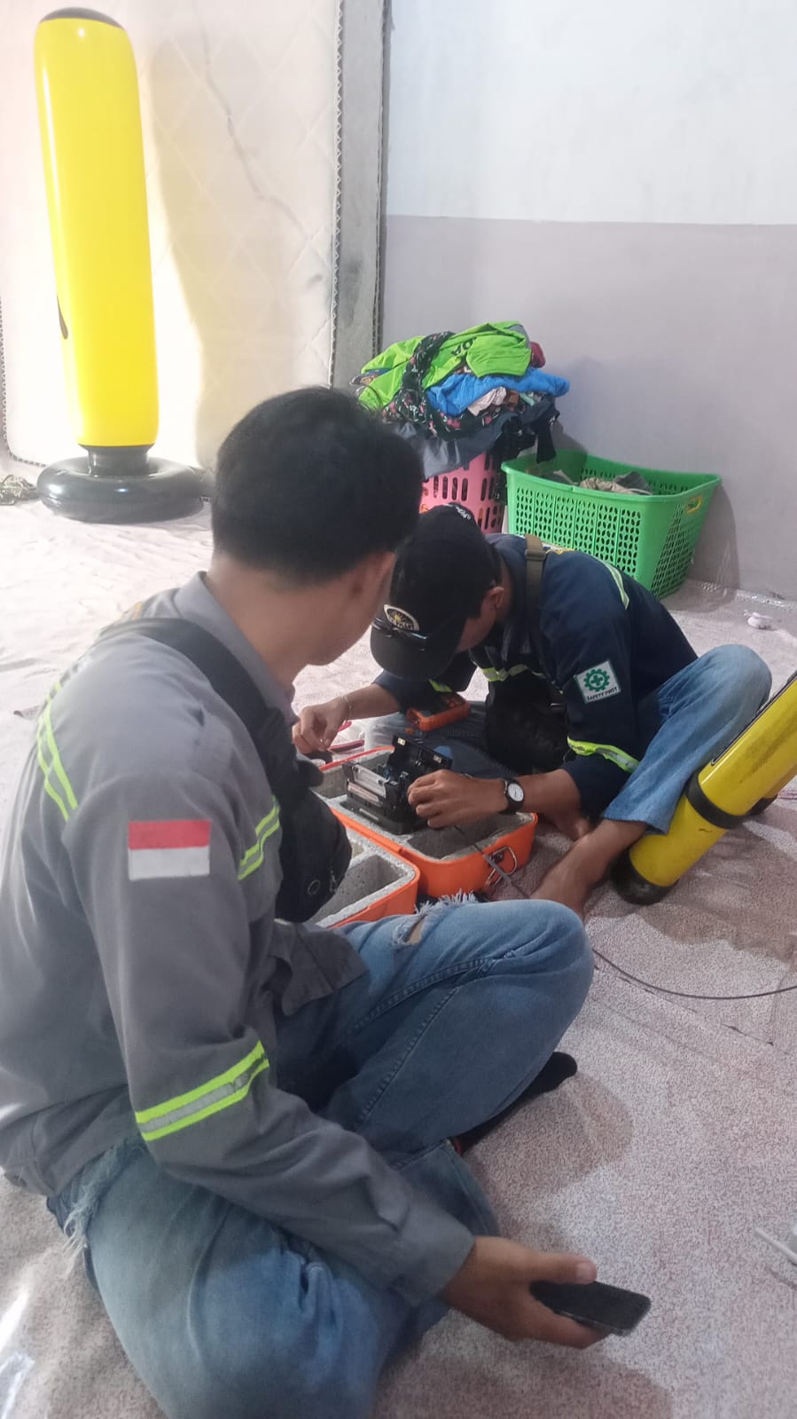 Dua teknisi mengerjakan penyambungan fiber optik di dalam ruangan